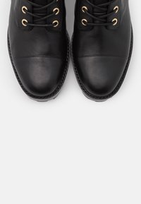 Botas de cuero negro hasta el tobillo con punteras redondeadas, ojetes dorados para los cordones y costura en contraste a lo largo de la suela. Suela plana y texturizada.