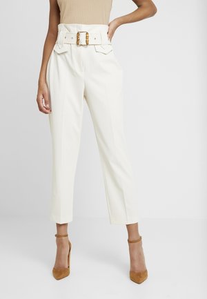 Witte high-waisted broek met een brede riem met gouden gesp, gestructureerd ontwerp en cropped zoom, gecombineerd met bruine hoge hakken.