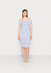 Vestido com padrão floral em azul claro, com mangas bufantes transparentes, corpete ajustado e bainha em camadas com babados. Usado com sandálias brancas com tiras.