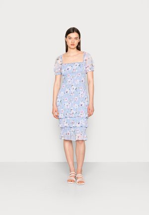 Vestido com padrão floral em azul claro, com mangas bufantes transparentes, corpete ajustado e bainha em camadas com babados. Usado com sandálias brancas com tiras.