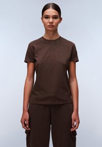 T-shirt in cotone marrone con collo rotondo e maniche corte, caratterizzato da una vestibilità comoda e dettagli di cucitura sottili. Indossato con pantaloni abbinati.