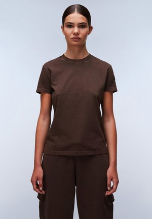 Braunes Baumwoll-T-Shirt mit Rundhalsausschnitt und kurzen Ärmeln, featuring einen lockeren Schnitt und dezente Stickdetails. Trägt passende Hosen.