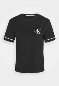 Svart bomullst-shirt med kort ärm och vita accentstrimmor på ärmarna. Har en liten vit "ck"-logotyp på vänster bröst.