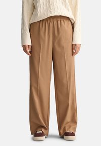 Pantalones beige de pierna ancha con cintura elástica, con una textura suave. Combinados con un suéter de punto color crema y zapatos oscuros.