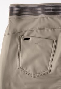 Beige läderbyxor med en grå randig midjeband och en bakficka med en metallisk logotyp. Sletten yta med precisa sömnadsdetaljer.