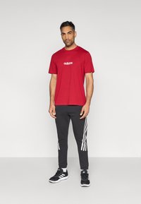 Punane puuvillane t-särk valge "adidas" logoga, kombineeritud mustade jogger-pükstega, mille külgedel on valged triibud. Mustad tossud.