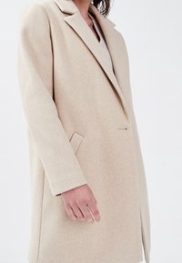 Beige uldblandingsfrakke med klippet krave, enkelt knaplukning og sidelommer. Glat tekstur, skræddersyet pasform med en lige silhuet.