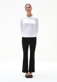 Biała koszula z długim rękawem w połączeniu z czarnymi żebrowanymi spodniami dzwonowymi. Look dopełniają teksturowane czarne buty i minimalistyczne dodatki.