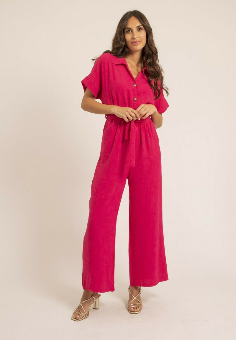 Combinaison fuchsia à manches courtes, devant boutonné, taille cintrée et design à jambes larges. Fabriquée en tissu léger, avec une finition texturée.