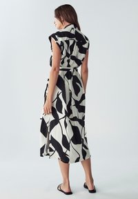 Abito midi a fantasia bianco e nero con maniche a cappuccio, vita con cintura e fessure laterali, realizzato in tessuto leggero.