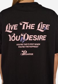 Black cotton t-shirt featuring pink text: "Live The Life You Desire" and "You’re The Flyest When You’re The Happiest," with butterfly graphics.