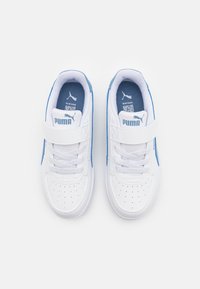 Zapatillas blancas de textura suave, con acentos azules, perforaciones para transpiración y una correa de velcro sobre los cordones.