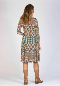 Flerfärgad mönstrad klänning med trekvartsärmar, en figurnära midja och en svängd kjol; tillsammans med bruna knäskor.