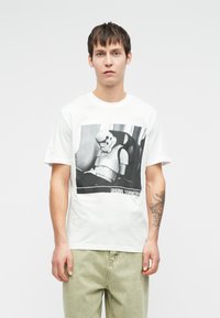 Bela bomba iz bombažne majice z črno-belo grafiko Stormtrooperja in besedilom "ORIGINAL STORMTROOPER" na dnu.