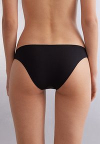 Schwarze Baumwoll-Bikiniunterwäsche mit einem tief sitzenden Schnitt, glatter Textur und minimaler Naht an den Kanten für einen nahtlosen Look.