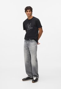 Melns īsām piedurknēm T-krekls ar baltu punktiņu logotipu, kombinēts ar gaiši pelēkiem taisnajiem džinsiem un melnām kedām ar baltām kurpēm.