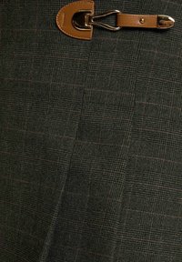 Tessuto a quadri verde scuro con sottili linee rosse, dotato di una tracolla in pelle marrone e dettagli con fibbia dorata.