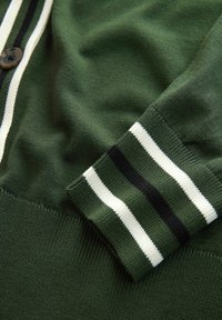 Grüne Strickjacke mit Knopfverschluss, mit einem gerippten Bündchen, das schwarze, weiße und grüne Streifen zeigt. Weiche Textur und figurbetontes Design.