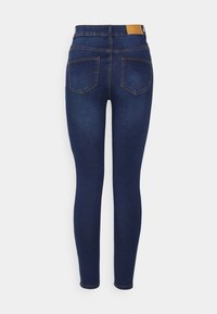 Jeans ajustados de color azul oscuro con una cintura alta, que cuentan con dos bolsillos traseros, costuras en contraste y una etiqueta de cuero marrón en la cintura.