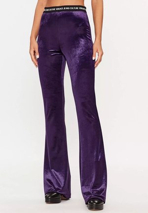 Lila samtige Schlaghose mit schwarzem elastischem Bund von Versace Jeans Couture, getragen mit schwarzen Plateauschuhen.