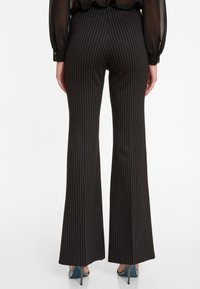 Zwarte uitlopende broek met smalle witte streepjes, met een gladde textuur en een middelhoge taille. De lengte reikt tot de enkel en onthult hakken.