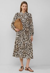 Leopardprint jurk met een kraagontwerp, lange mouwen, een gelaagd rokje en een vloeiende pasvorm. Gecombineerd met een geweven bruine tas en platte sandalen.