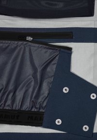 Sac bleu marine avec un extérieur texturé, comprenant un compartiment zippé, une quincaillerie en argent et une bandoulière noire de marque. Doublure douce visible à l'intérieur.