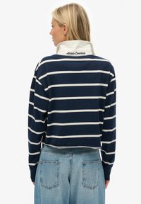 Marineblauw-wit gestreept top met lange mouwen en een kraag, met "Athletic Essentials" geborduurd op de achterkant. Casual pasvorm.