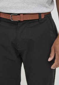 Svarte bukser med en glatt tekstur, med et brunt lærbelte med en metallspenne. Designet har rette snitt og minimal søm.