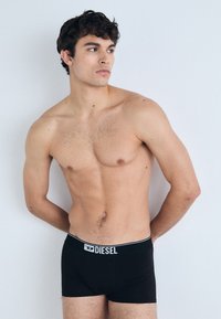 Black boxer briefs made of stretchy fabric, featuring a contrasting elastic waistband with "DIESEL" logo in white. Simple and fitted design.