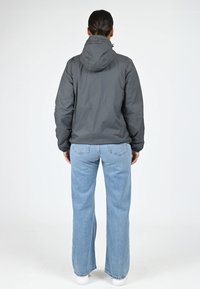 Grijze hoodiejas van lichtgewicht materiaal, met een ontspannen pasvorm en elastische manchetten, gecombineerd met lichtblauwe wijdne zijden jeans.