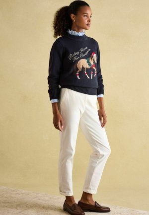 Navy sweater with horse design and "Riding Home For Christmas" text. Paired with white pants and brown loafers. Ruffled collar visible.