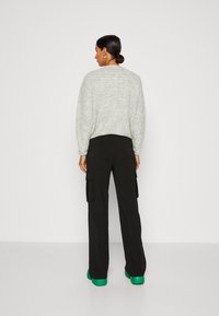 Light gray sweater, loose fit, crew neckline. Black cargo pants with side pockets. Green platform shoes. Plain background.