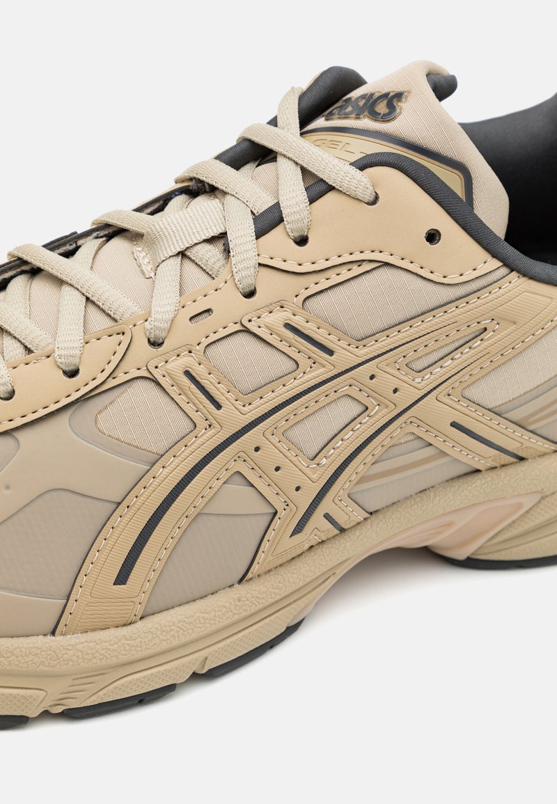 Baskets de sport beige présentant un design léger, des matériaux texturés, des accents noirs prononcés et une semelle rembourrée pour un bon soutien.