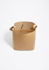 Torebka typu tote w odcieniu brązowym, o gładkiej fakturze, z szerokim brzegiem i pojedynczym paskiem na ramię. Wnętrze charakteryzuje się minimalistycznym designem bez przegródek.