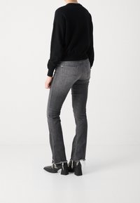 Schwarzer Pullover mit überschnittenen Schultern, kombiniert mit grauen Jeans mit fransigen Säumen und einem Slim Fit. Schwarze Stiefeletten runden den Look ab.