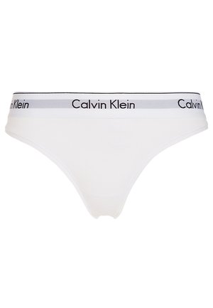 Thong din bumbac alb cu un elastic negru și gri la talie, având inscripționat „Calvin Klein” în text repetat. Textură netedă, design minimal.