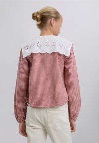 Red and white checked shirt with a white embroidered lace collar, long sleeves, and a relaxed fit. The back features a downward seam for added design.