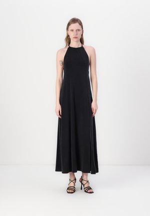 Black halter neck maxi dress featuring a flowing design, soft texture, and elegant silhouette. Paired with strappy black heels.