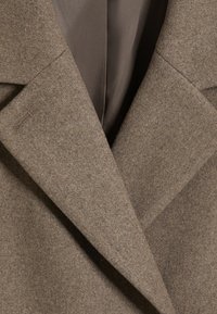 Gros plan d’un revers de manteau en laine marron avec des coutures visibles et un tissu de doublure intérieure lisse.