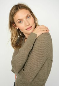 Pulover rib accesat de culoare verde măslinie, cu decolteu în V și mâneci lungi, având un detaliu cu nasture pe manșetă și un material moale, texturat.