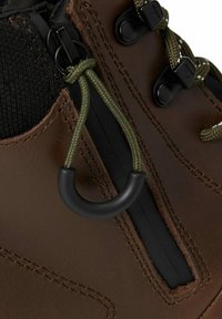 Botte en cuir marron avec des lacets verts enfilés à travers des œillets noirs et un verrou noir pour le serrage près de la couture.