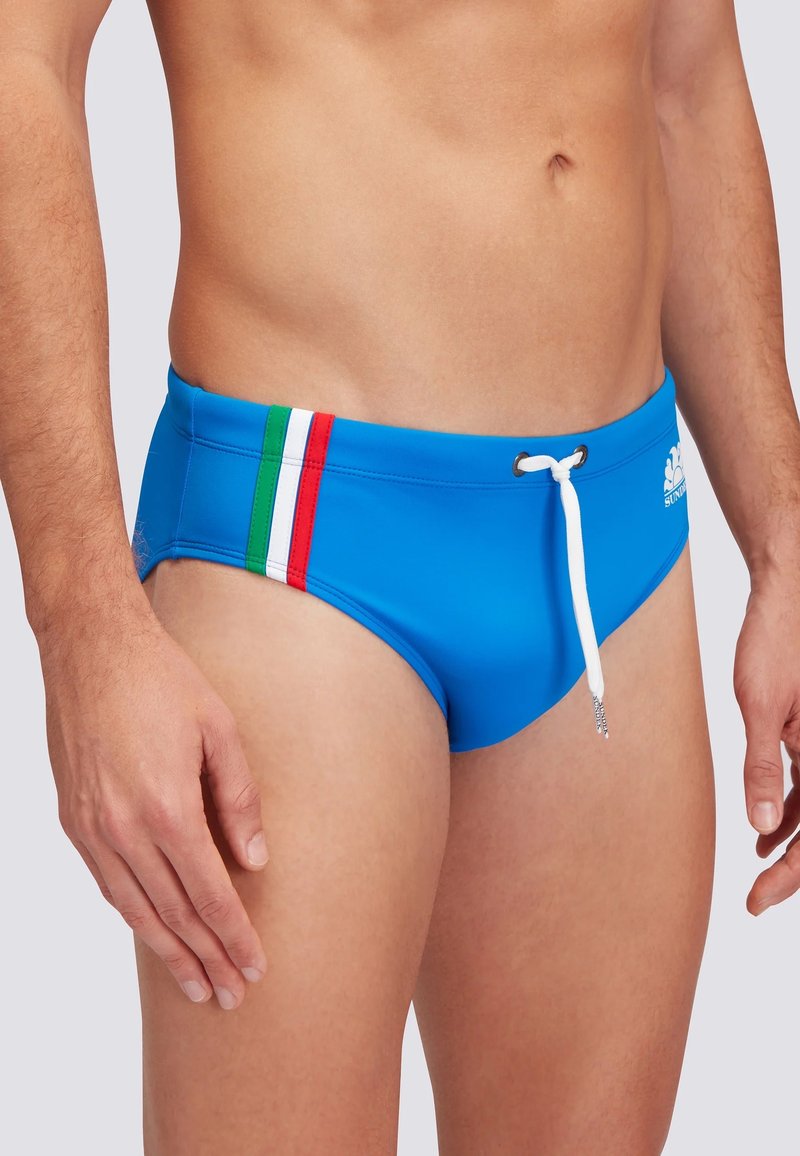 Slip da bagno blu realizzato in tessuto liscio, con un laccetto bianco e tre strisce verde, bianco e rosso lungo il lato.