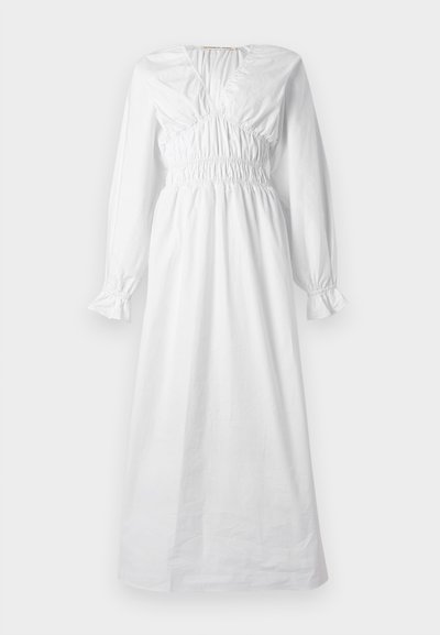 Μακρύ λευκό φόρεμα με μακριά μανίκια, σφηκωτή μέση και στήθος, μανσέτες με βολάν και λαιμόκοψη σε σχήμα V.