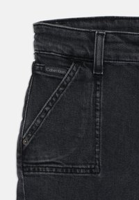 Jeans de mezclilla negra con un bolsillo frontal y una etiqueta de Calvin Klein. La tela tiene una textura suave con detalles de costura visibles.