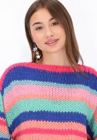 Pestrý pletený svetr s horizontálními pruhy v růžové, modré, zelené a broskvové barvě. Modelka má na sobě lesklé náušnice ve tvaru hvězdy.