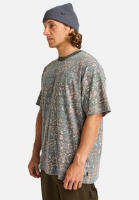 Camiseta de manga corta, gris con un patrón de diseños abstractos en colores pastel; presenta un cuello redondo y una pequeña etiqueta de logo en el costado.
