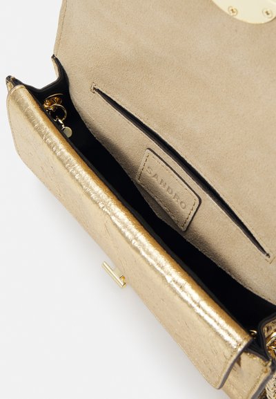 Zlatá metalická kabelka typu clutch s semišovým interiérem, s hladkým povrchem, značkovou etiketou a bezpečným zapínáním.