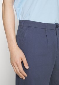 Mörkblå byxor i en bomullsblandning, med platt front, två sidofickor och knappstängning vid midjan.