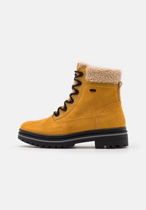 Geel suede laars met een romige bontkraag, zwarte veters en een robuuste zool. Kenmerkt stiksels en een ronde hakontwerp.